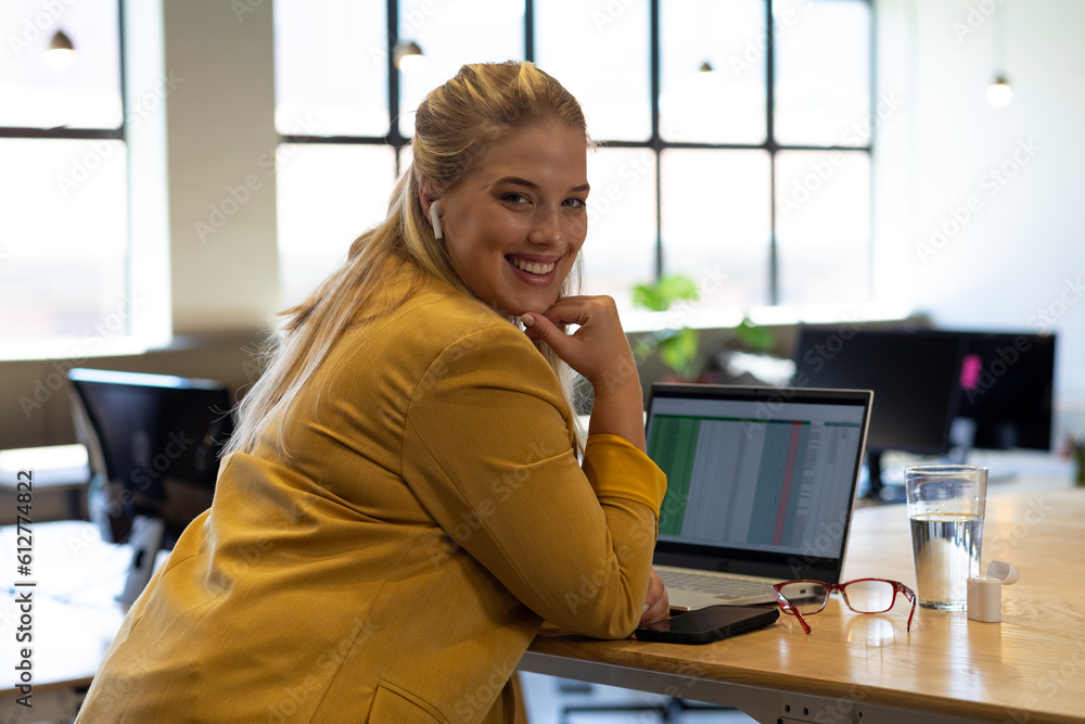 Wall mural Portrait of happy plus size caucasian casual businesswoman with laptop at desk