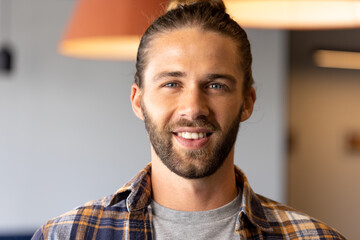 Portrait of happy caucasian casual businessman with hair bun smiling in office