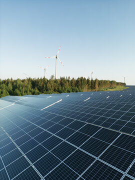Photovoltaik-Anlage in gr&uuml;ner Landschaft mit Windr&auml;dern im Hintergrund bei Sonnenschein