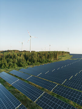 Photovoltaik-Anlage in gr&uuml;ner Landschaft mit Windr&auml;dern im Hintergrund bei Sonnenschein