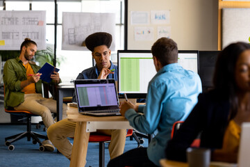 Diverse male and female creative colleagues working with computers in office