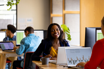 Happy casual businesswoman and diverse colleagues working using computers in office