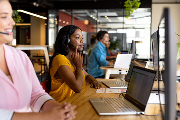 Diverse male and female creative colleagues working using phone headsets and computers in office