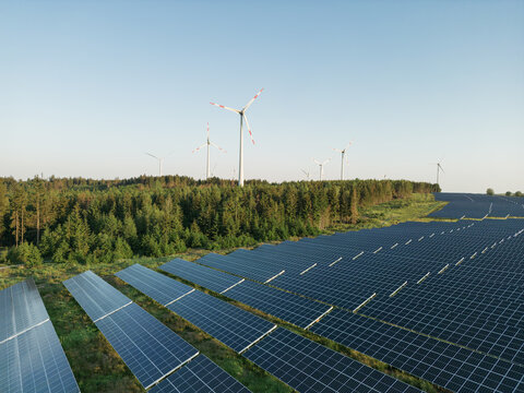 Photovoltaik-Anlage in gr&uuml;ner Landschaft mit Windr&auml;dern im Hintergrund bei Sonnenschein