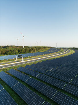 Autobahn zwischen Photovoltaik-Anlagen mit Windr&auml;dern im Hintergrund in gr&uuml;ner Natur bei Sonnenschein