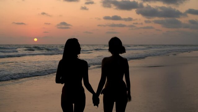Holiday concept of 4k Resolution. The silhouette of two girls walking on the beach.