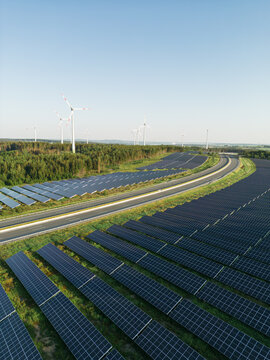 Autobahn zwischen Photovoltaik-Anlagen mit Windr&auml;dern im Hintergrund in gr&uuml;ner Natur bei Sonnenschein