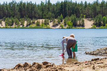 Fototapeta na wymiar Fitness Mom and her little daughter play in the water on a forest lake on a summer day.