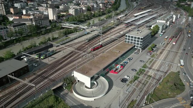 The train station in the city of Brig in Valais Switzerland. There is a locomotive driving into the station and cars driving on the streets