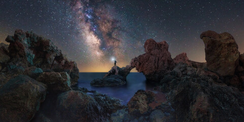Milky way over the Amalia arch. A man with a lantern is watching the Milky Way over the famous Amalia arch. The arch is inside a rock formation and also inside the sea. Cartagena, Murcia, Spain © Revive Photo Media