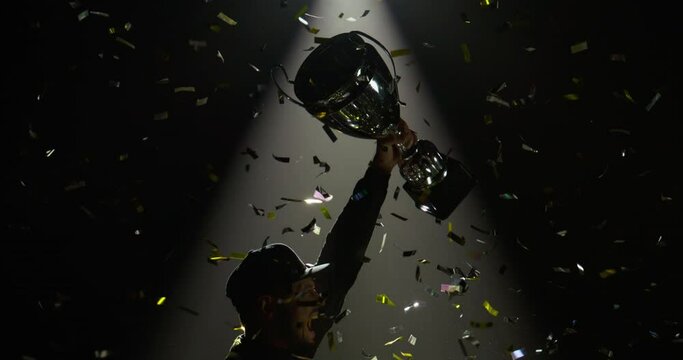 Silhouette of race car driver celebrating the win in a race against bright stadium lights, rising a trophy over his head