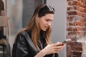 Portrait of happy female dressed casually holding mobile phone, typing messages, communicating with...