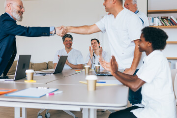 doctors compliment each other by shaking hands to the applause of their colleagues
