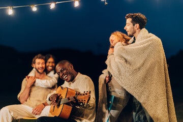 friends sing with guitar around the fire in a summer party