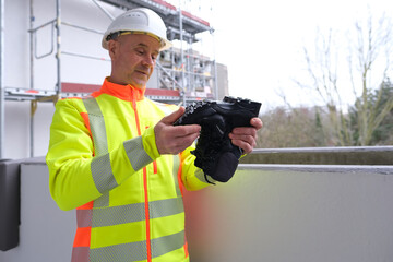 black work boots made of leather with reinforced cape, high top in hands of man, mature male mature builder, worker in yellow work clothes testing special protective professional shoes, for mountains