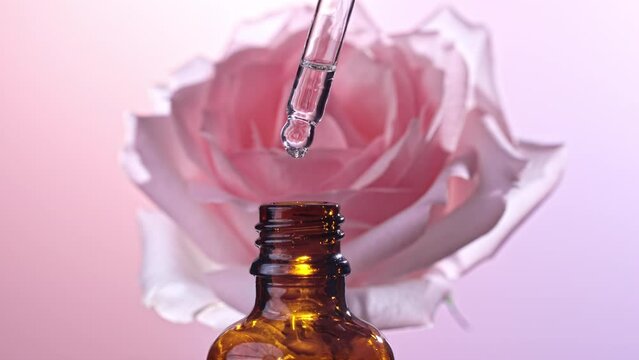 Rose essential oil falling from glass dropper into a cosmetic bottle