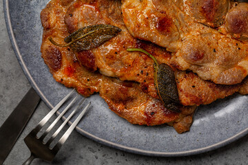 Close-up of fried pork steaks, cuts with spices and sage. Copy space, grey background.