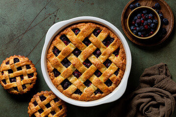 Whole baked mixed berry crust pie or tart with lattice, mini tarts. Homemade, fresh berries. Green table surface, directly above. © Olga