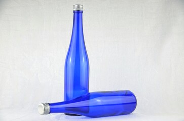 Two blue bottles with silver caps (mockup), one is standing, the other one lies in front of the other on a white background
