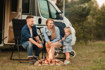 A family cooks sausages on a bonfire near their motorhome in the woods