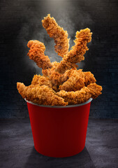 Fried chicken Hot crispy strips crunchy pieces of chicken breast tenders in a Bucket - a large Red box on the black table in the restaurant 