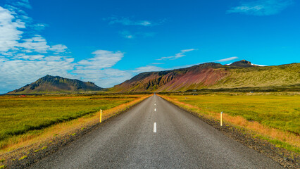 Fototapeta na wymiar Panoramic over a paved road and Icelandic colorful and wild landscape with fjords and sea at summer time, West Iceland