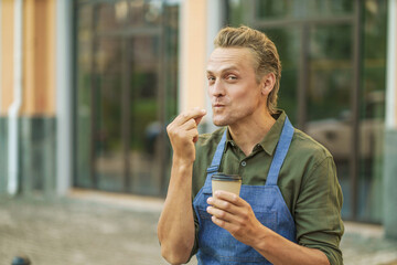 Barista wearing apron, demonstrating delicious taste of hot coffee by kissing fingers in Italian-style gesture. Background features urban cityscape, creating vibrant and dynamic atmosphere. 