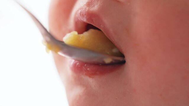 grimy baby eats from a spoon close-up of the lips. happy family kid dream concept. baby close-up eats with a dirty spoon. baby opens mouth eats mashed potatoes from a spoon lifestyle