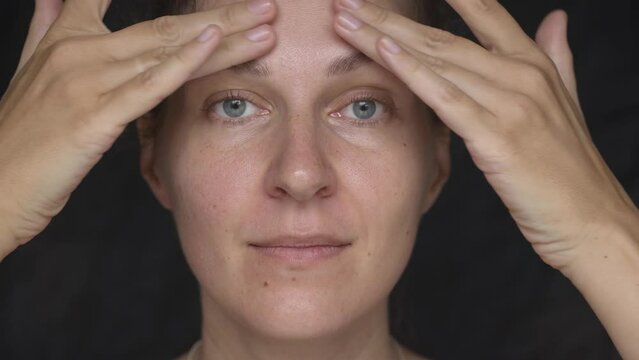 Close-up of young attractive woman without makeup touches her face with her fingers, she is happy with her appearance, looks at the camera 4K