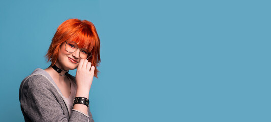 Portrait of stylish cheerful teenage girl with makeup in headphones on blue background.Large banner with negative space.