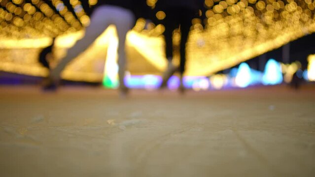 Back view female feet riding ice skates in slow motion to blur. Two graceful Caucasian young sportswomen training on ice rink on Christmas eve in night city