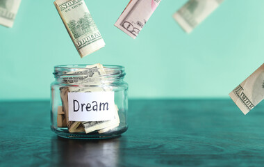 Save money for a dream. Glass jar with dollars on a wooden table. Piggy bank with banknotes and dollars flying around. Copy space. The concept of financial savings