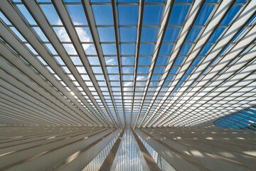 White steel and glass structures illuminated by sun. Vivid light and shadow pattern, wide angle. Abstract graphic background with lines, diagonals and curves and summer blue sky with clouds behind.