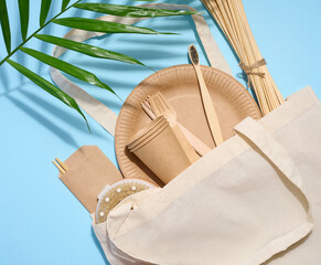 White cotton bag, wooden forks, plates and cups on a blue background. Waste recycling concept, zero...