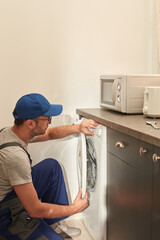 Handyman fixing broken washing machine in the apartment.