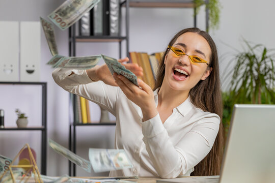 Cheerful rich young Caucasian business woman working on laptop and wasting throwing money to camera more tips earnings big profit success win lottery shopping. Happy freelancer girl at office desk