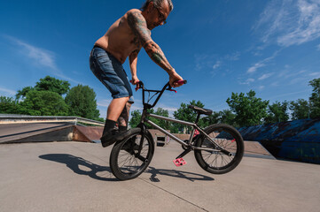 Fototapeta na wymiar A mature shirtless bike rider is performing tricks on a bmx in a skate park.