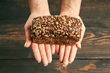 Loaf of fresh made rye multigrain bread in woman hands on wooden table background