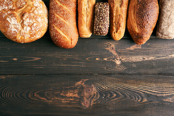 Different types of bread loaves on wooden background with copy space