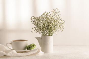 Coffee, macaroons, gypsophila bouquet on a white table. Cozy spring breakfast.