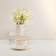 Coffee, a bouquet of gypsophila and a stack of books on a white table. Cozy breakfast.
