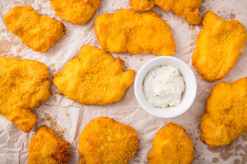 Small chicken schnitzel on baking sheet with herb mayonnaise