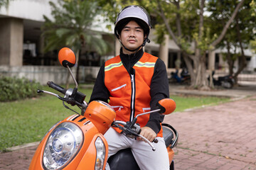 Happy young Thai motorcycle taxi driver or rider waiting for passenger near by the building in the city.