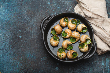 Escargots de Bourgogne Snails with Garlic Butter and Parsley in black cast iron pan on rustic stone...