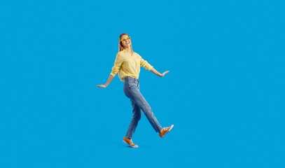 Fototapeta na wymiar Overjoyed funny millennial teenager girl isolated on blue studio background dancing. Smiling young woman in glasses and casual wear have fun make dancer moves. Entertainment concept.
