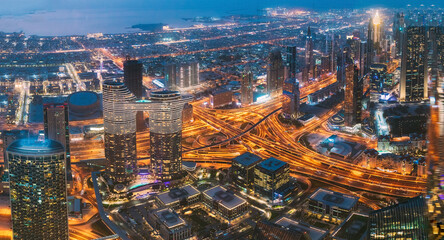 Aerial View Of Evening Night Scenic View Of Skyscraper In Dubai. Street Night Traffic In Dudai Skyline. Waterfront And Dubai Cityscape In Summer Evening Illuminations. Urban background. High quality