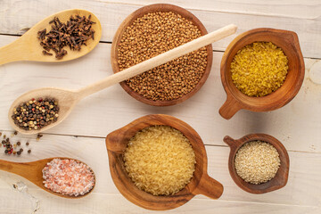 Dry cereals and seasonings in wooden cups with wooden spoons on a wooden table, macro, top view.