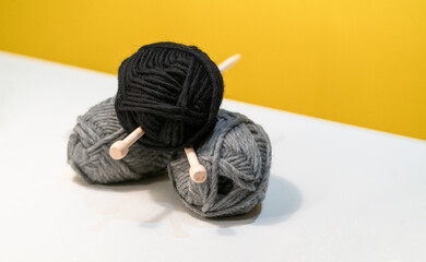 Yarn ball of black and grey wool thread for knitting with wooden spindle or needle on white table...