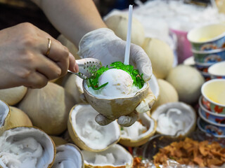 Hands serving white ice cream in coconut in the vietnamese night market and food festival