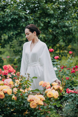 Young woman walking among roses in garden and enjoying by bloom.